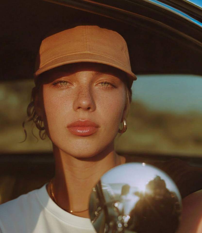 AI-generated portrait of a woman in a tan cap seen beside a car wing mirror, golden light