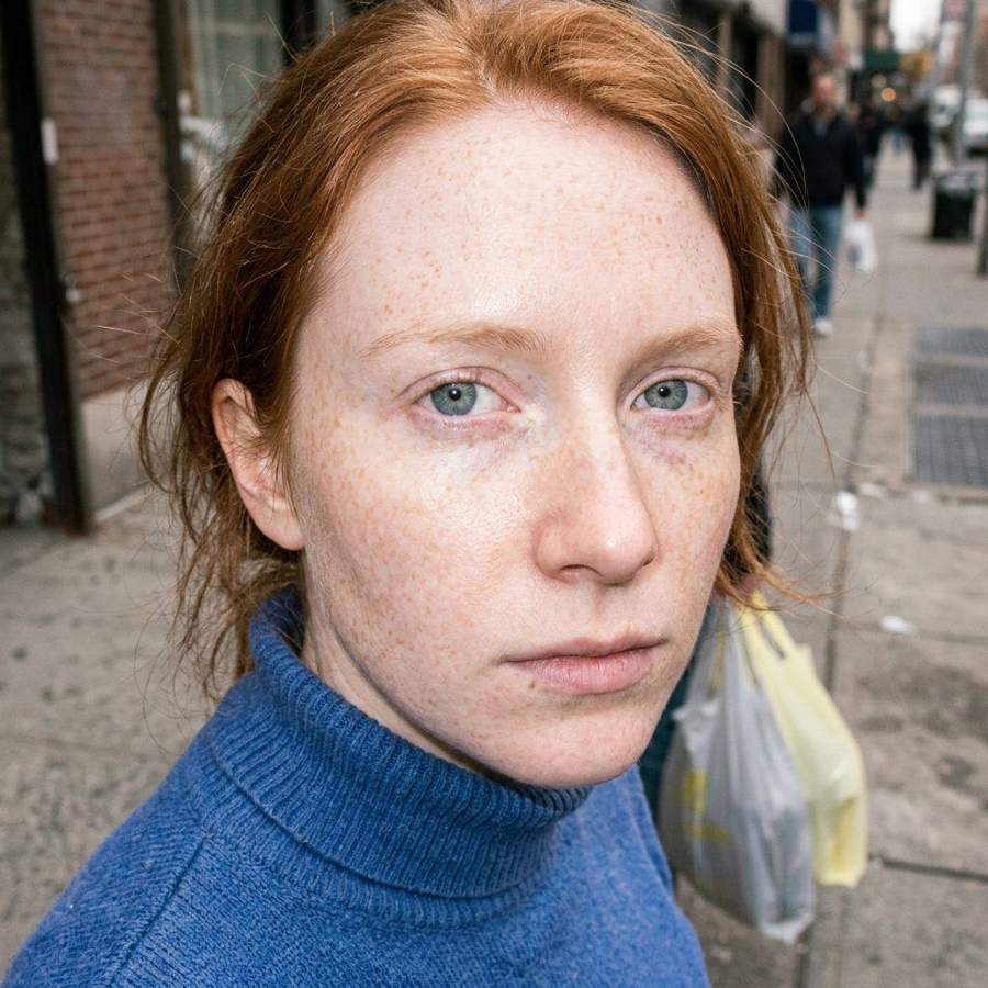 AI-generated street portrait of a freckled red-haired woman in a blue sweater
