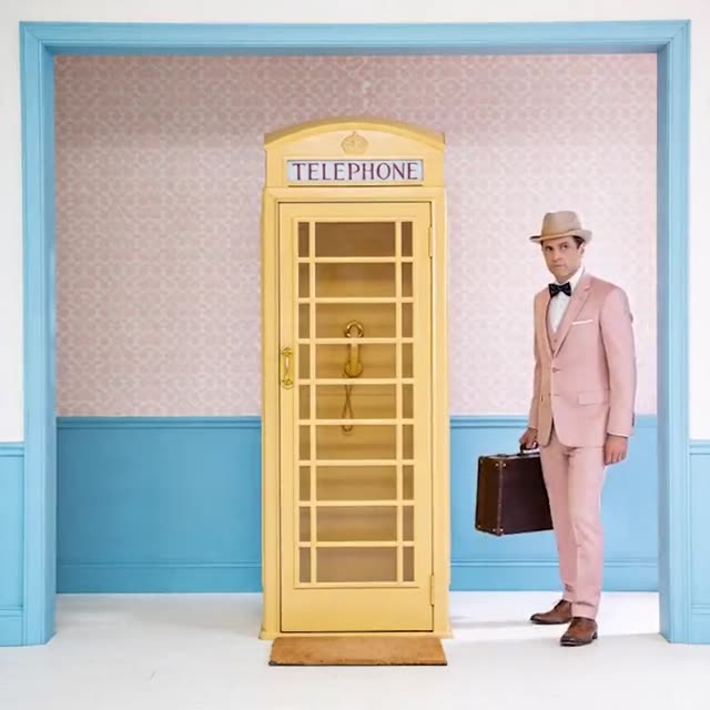 AI fashion film: a man in a pink suit with a suitcase beside a yellow telephone booth